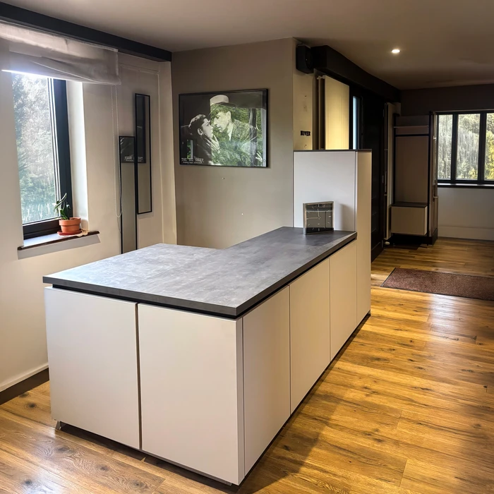 Showroom de cuisine moderne avec îlot central aux façades blanches laquées mat et plan de travail en céramique effet béton anthracite à bords droits