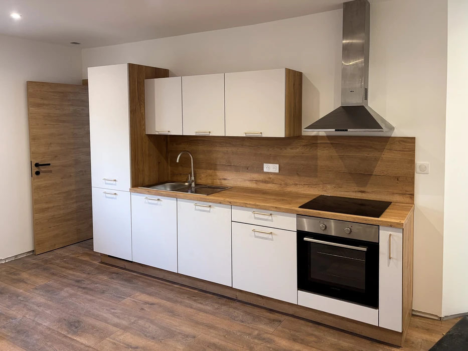 Cuisine moderne équipée en linéaire, armoires blanches laquées avec poignées dorées, plan de travail bois massif, crédence effet chêne